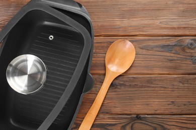 Photo of Black pot, spoon and glass lid on wooden table, flat lay. Space for text