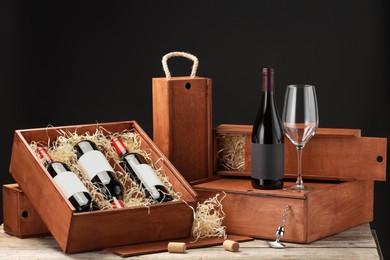 Photo of Boxes with wine bottles and glass on wooden table against black background