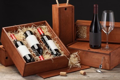 Boxes with wine bottles and glass on wooden table against black background