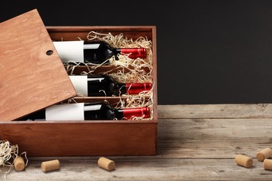 Photo of Box with wine bottles and corks on wooden table against black background. Space for text