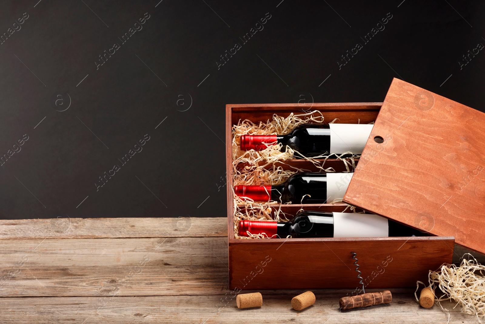 Photo of Box with wine bottles, corkscrew and corks on wooden table against black background. Space for text