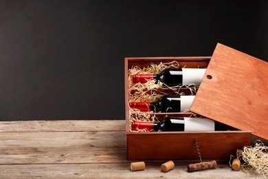 Photo of Box with wine bottles, corkscrew and corks on wooden table against black background. Space for text