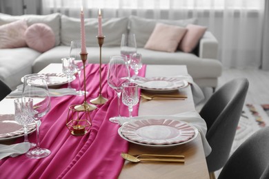 Photo of Beautiful table setting with burning candles and pink accent in dining room