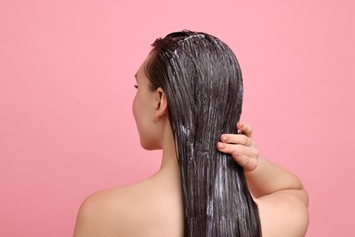 Woman applying hair mask on pink background, back view