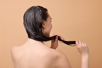 Woman applying hair mask on beige background, back view
