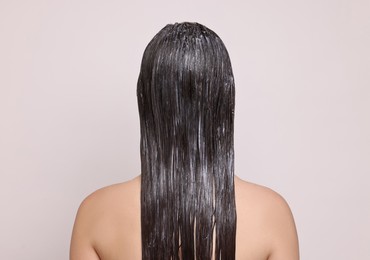 Woman with applied hair mask on light background, back view