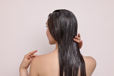 Woman applying hair mask on light background, back view