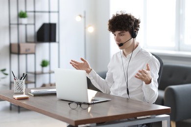 Photo of Teenager in headset having video chat via laptop at table indoors. Remote work