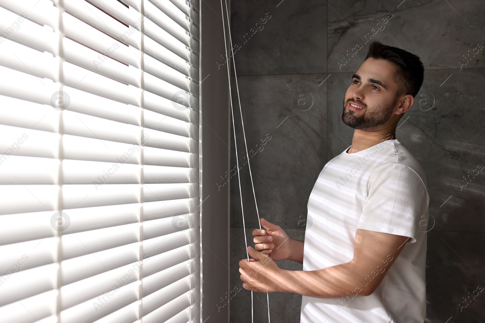 Photo of Man adjusting window blinds at home, space for text