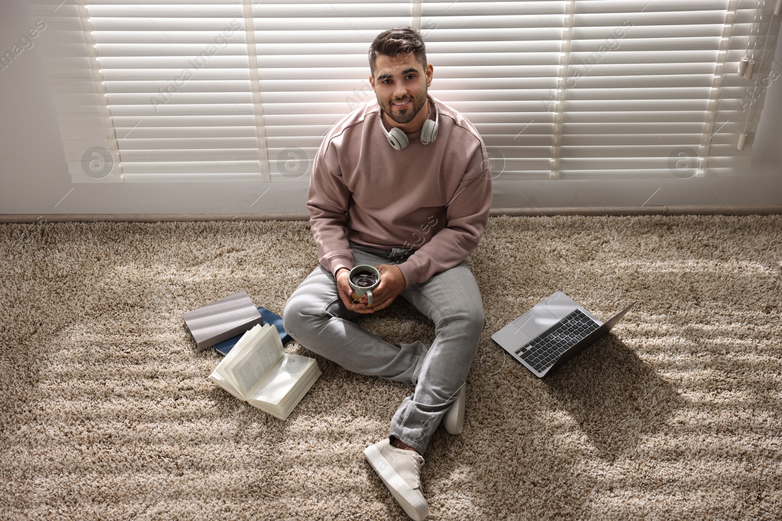 Photo of Man with laptop and books sitting near window blinds at home, above view