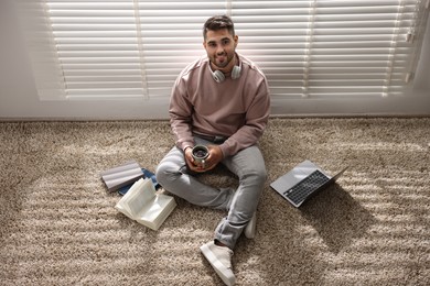 Man with laptop and books sitting near window blinds at home, above view