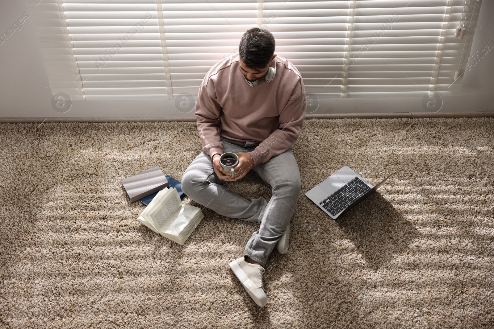 Photo of Man with laptop and books sitting near window blinds at home, above view