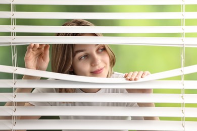 Photo of Young woman looking through window blinds on blurred background