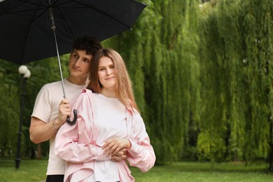 Photo of International dating. Lovely young couple with umbrella spending time together in park, space for text