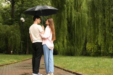 Photo of International dating. Lovely young couple with umbrella spending time together in park, space for text