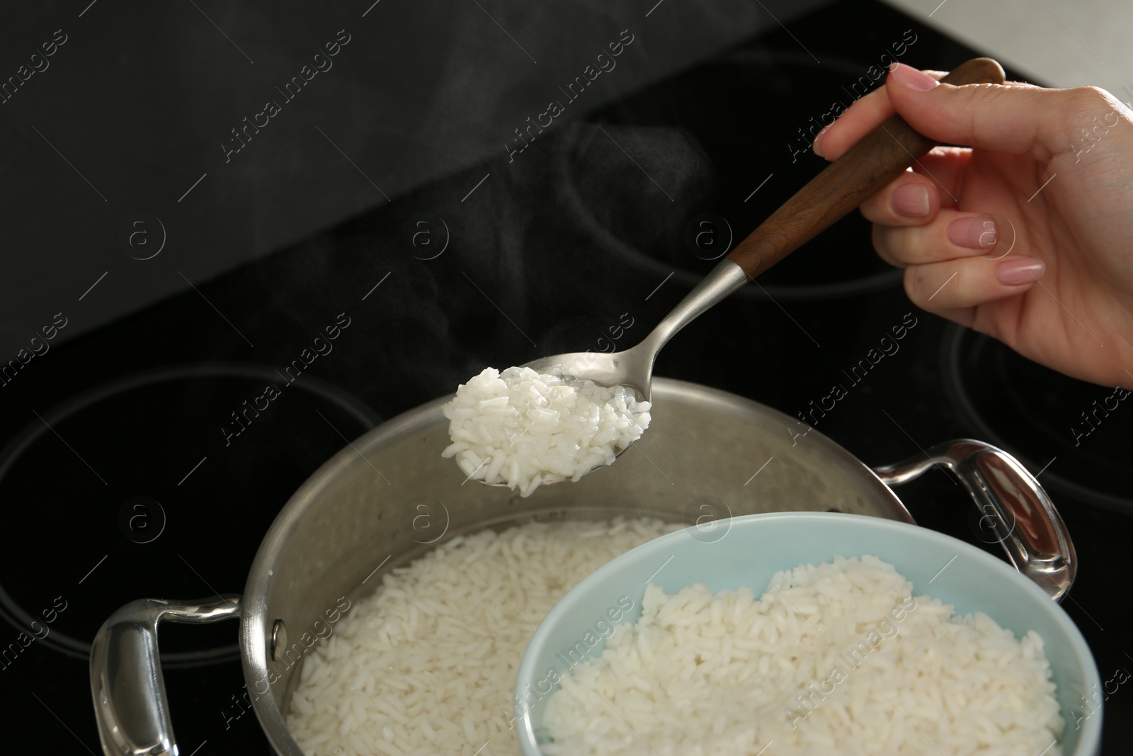 Photo of Woman taking boiled rice from pot into bowl, closeup