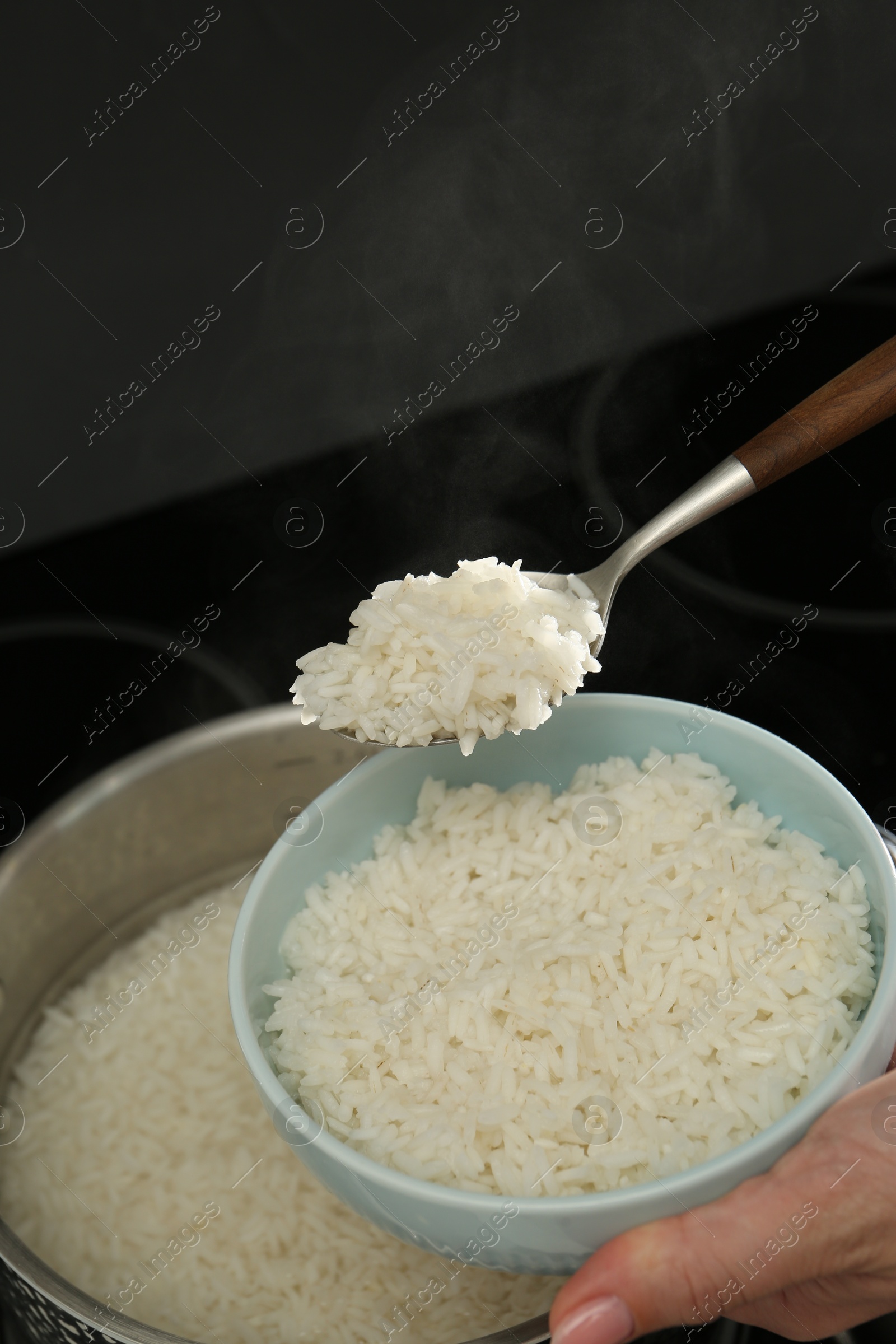 Photo of Woman taking boiled rice from pot into bowl, closeup