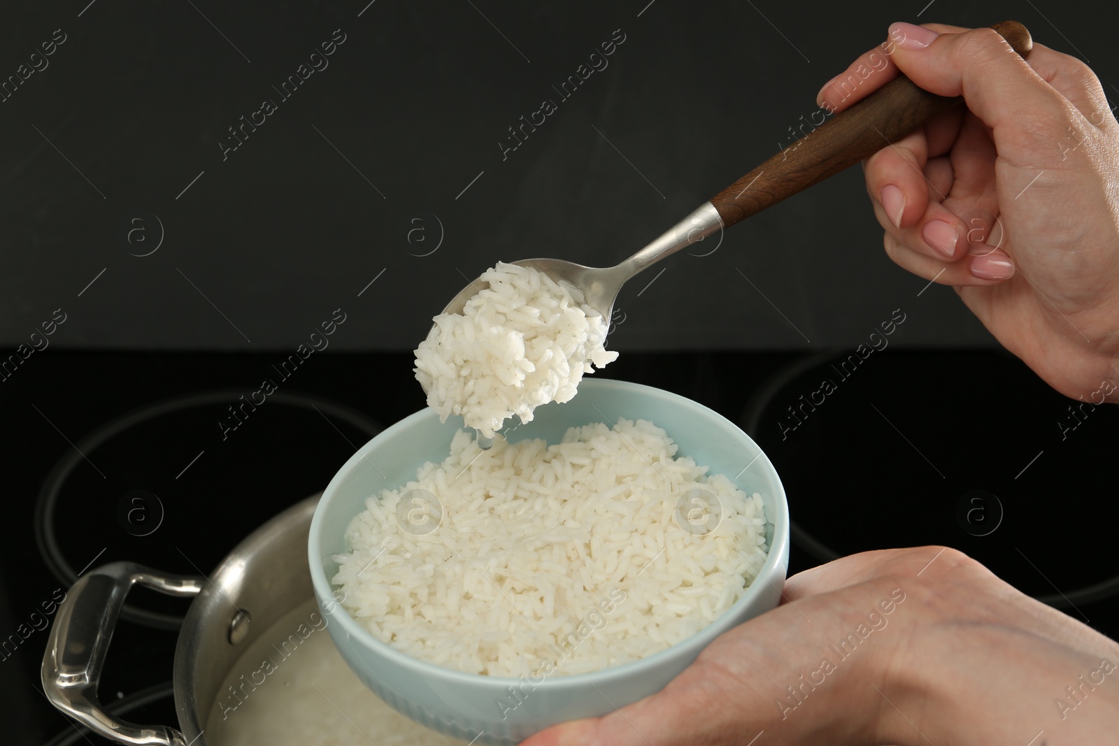 Photo of Woman taking boiled rice from pot into bowl, closeup