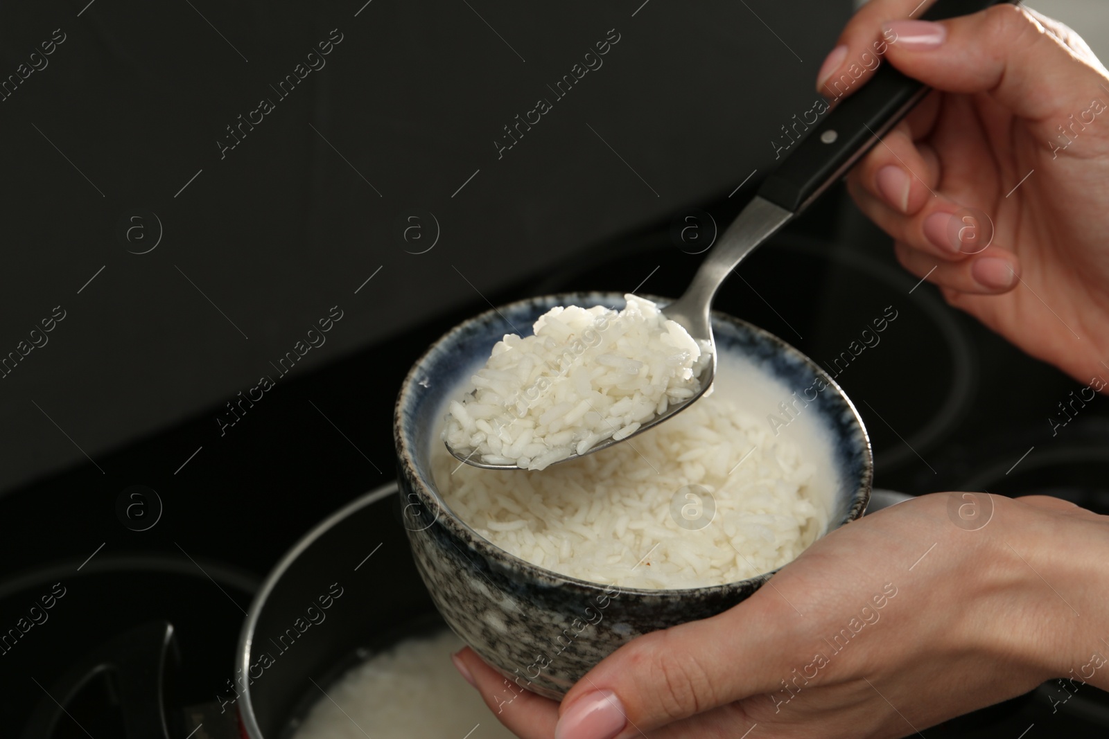 Photo of Woman taking boiled rice into bowl, closeup