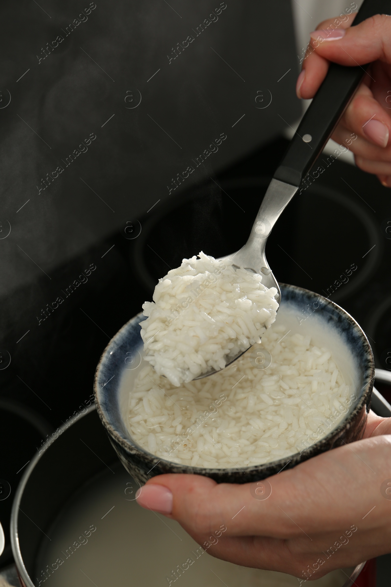 Photo of Woman taking boiled rice from pot into bowl, closeup