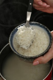 Woman taking boiled rice from pot into bowl, closeup