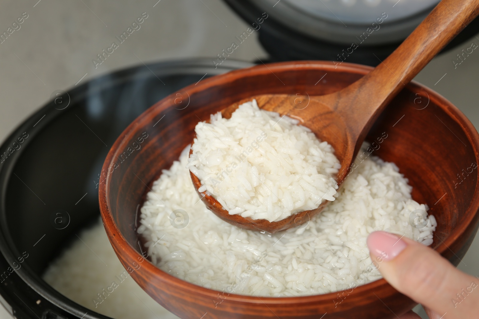 Photo of Woman taking boiled rice into bowl, closeup