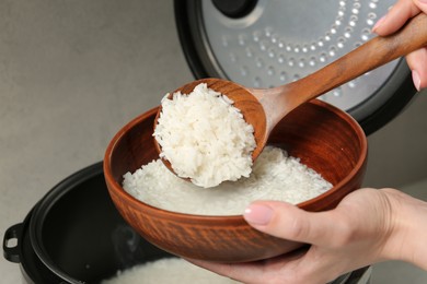 Photo of Woman taking boiled rice into bowl on grey background, closeup