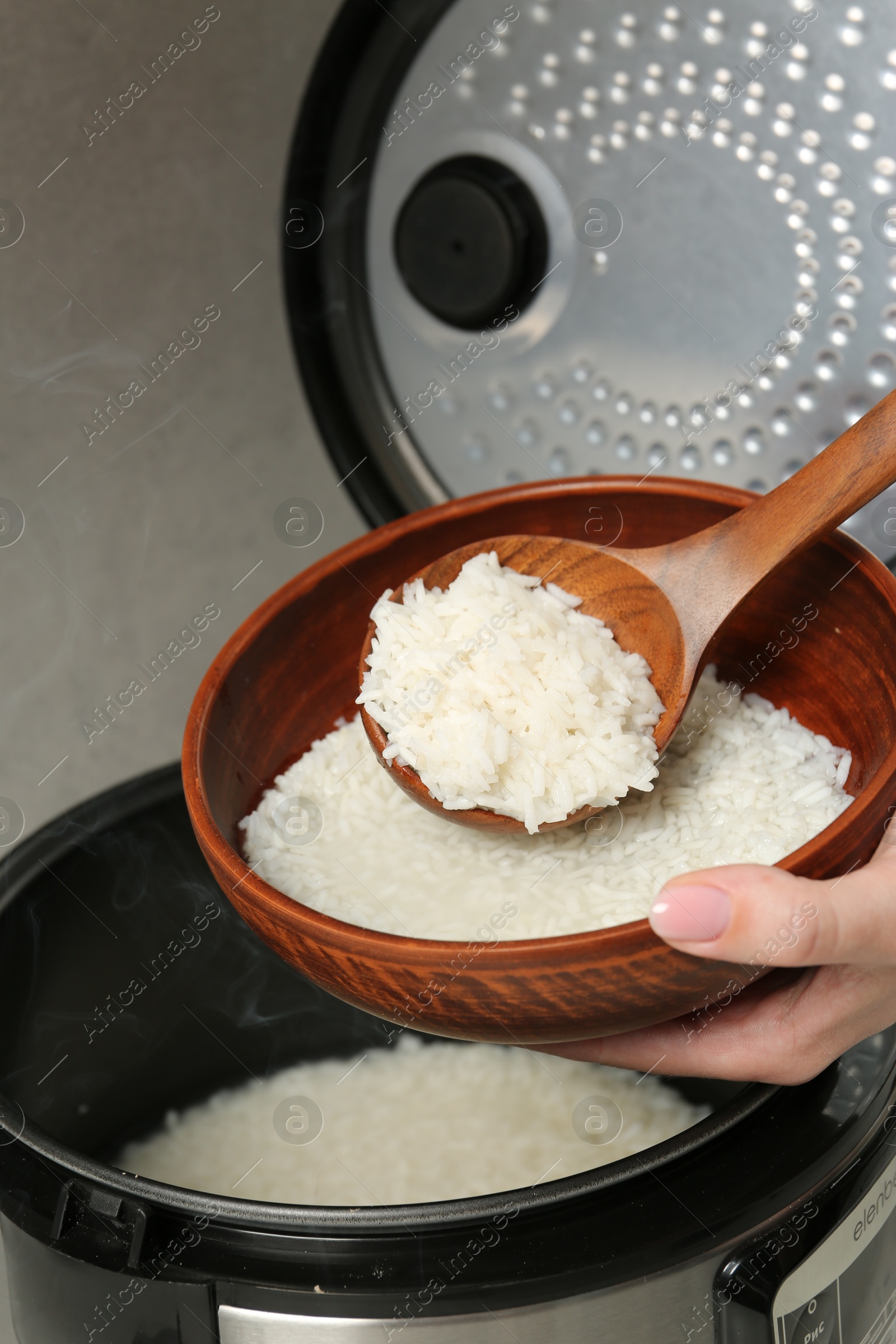 Photo of Woman taking boiled rice into bowl on grey background, closeup