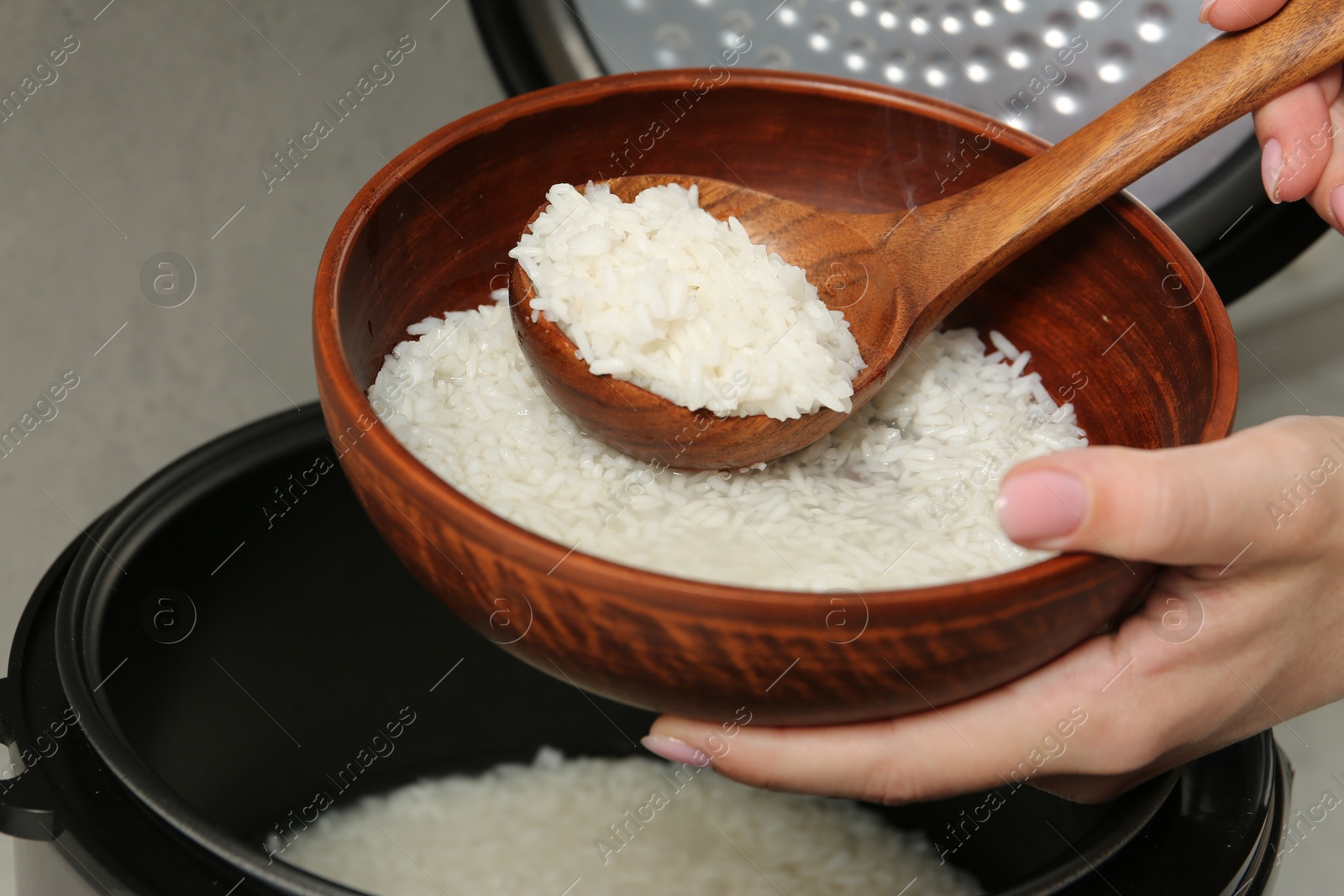 Photo of Woman taking boiled rice into bowl on grey background, closeup