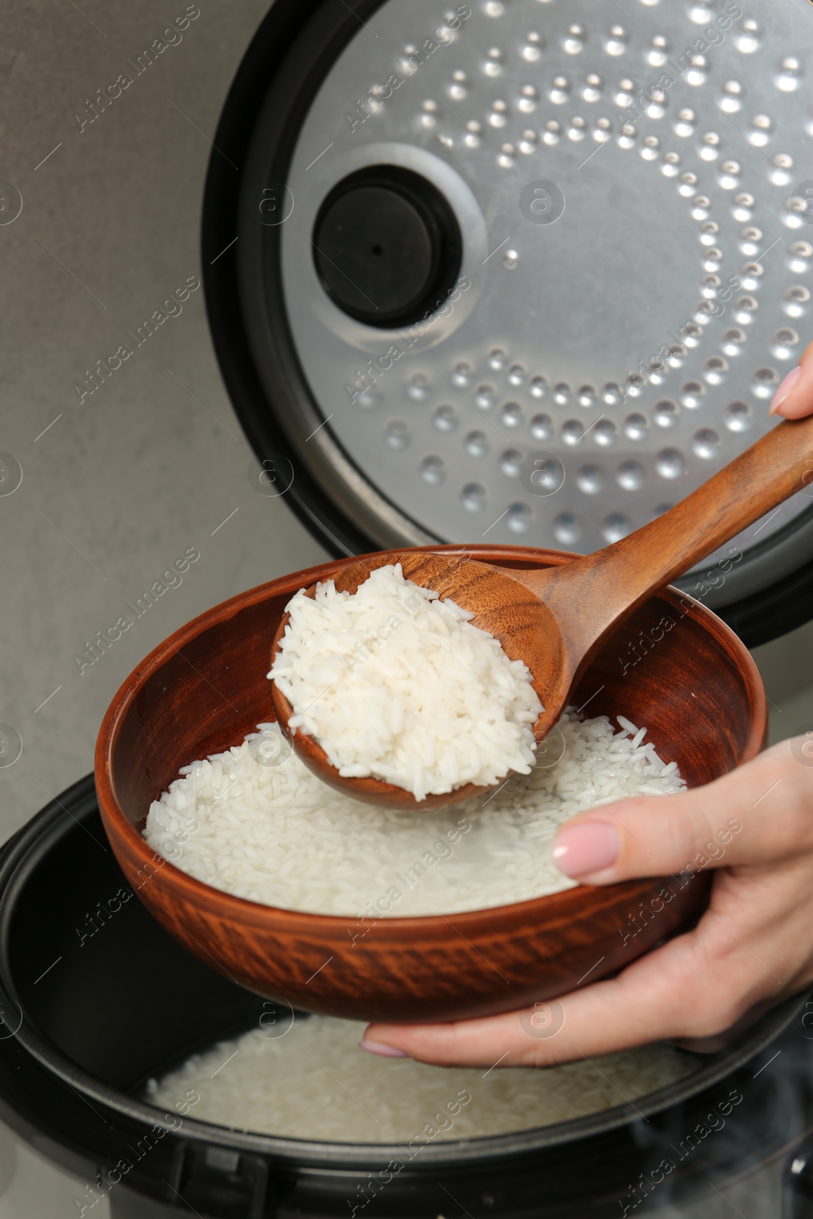 Photo of Woman taking boiled rice into bowl on grey background, closeup