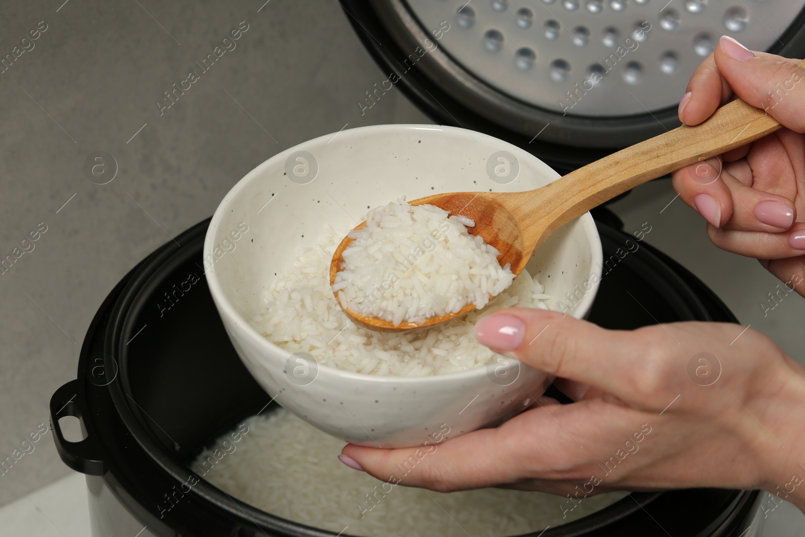 Photo of Woman taking boiled rice into bowl on grey background, closeup