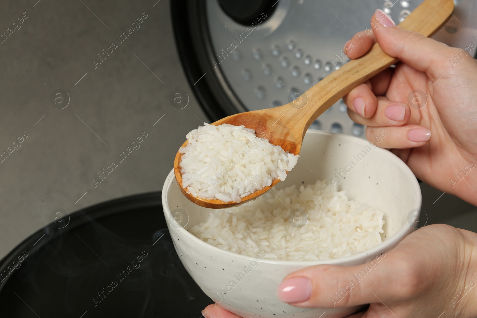 Photo of Woman taking boiled rice into bowl on grey background, closeup