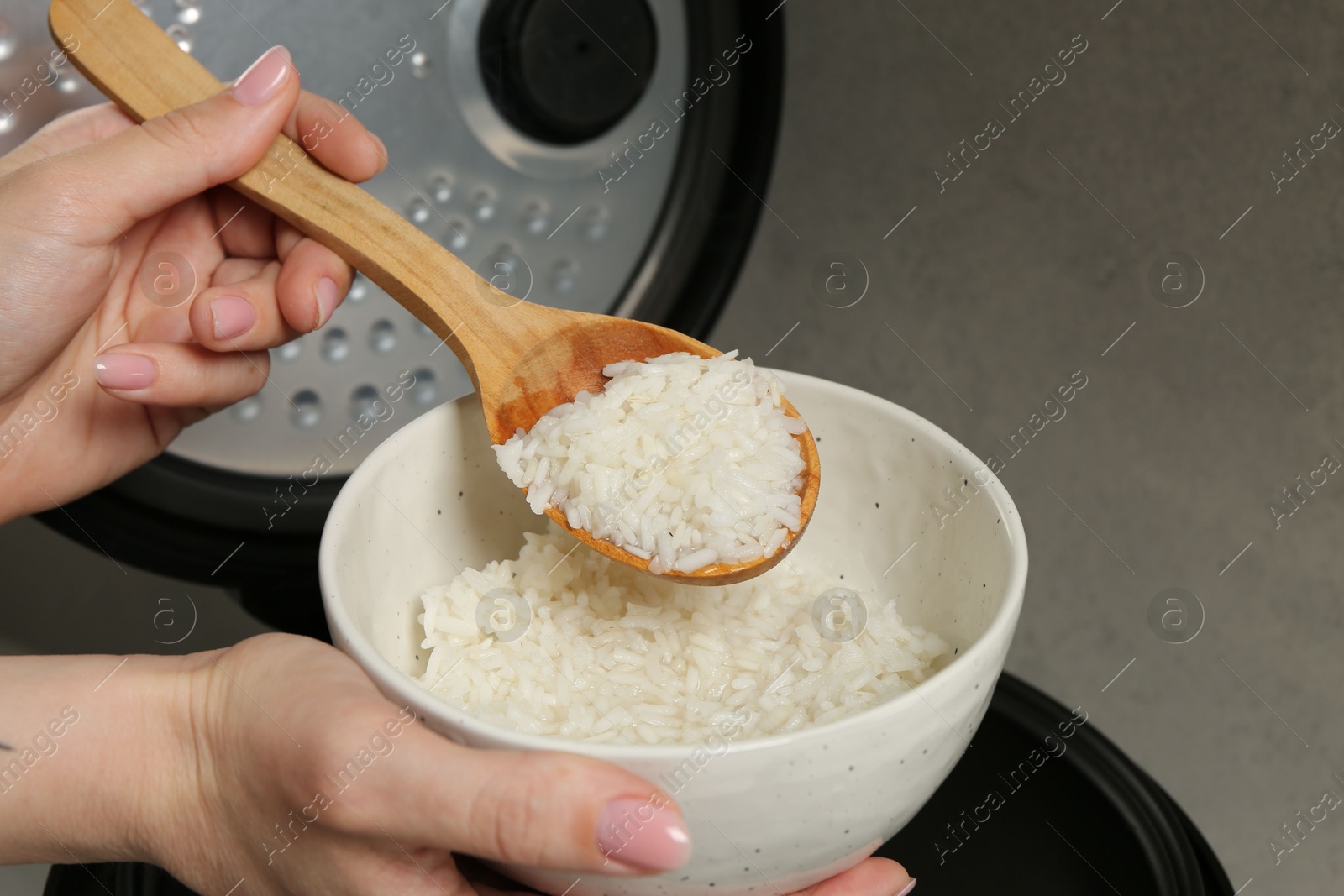 Photo of Woman taking boiled rice into bowl on grey background, closeup