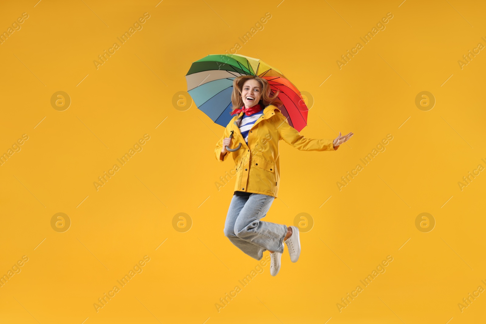 Photo of Woman with colorful umbrella jumping on yellow background