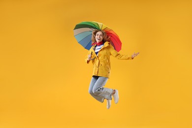 Woman with colorful umbrella jumping on yellow background