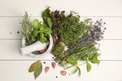 Different aromatic herbs, garlic, mortar and pestle on white wooden table, top view