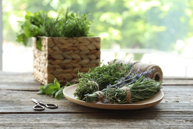 Photo of Different aromatic herbs and scissors on wooden table against blurred background