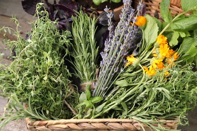 Photo of Different aromatic herbs in basket on wooden table, closeup