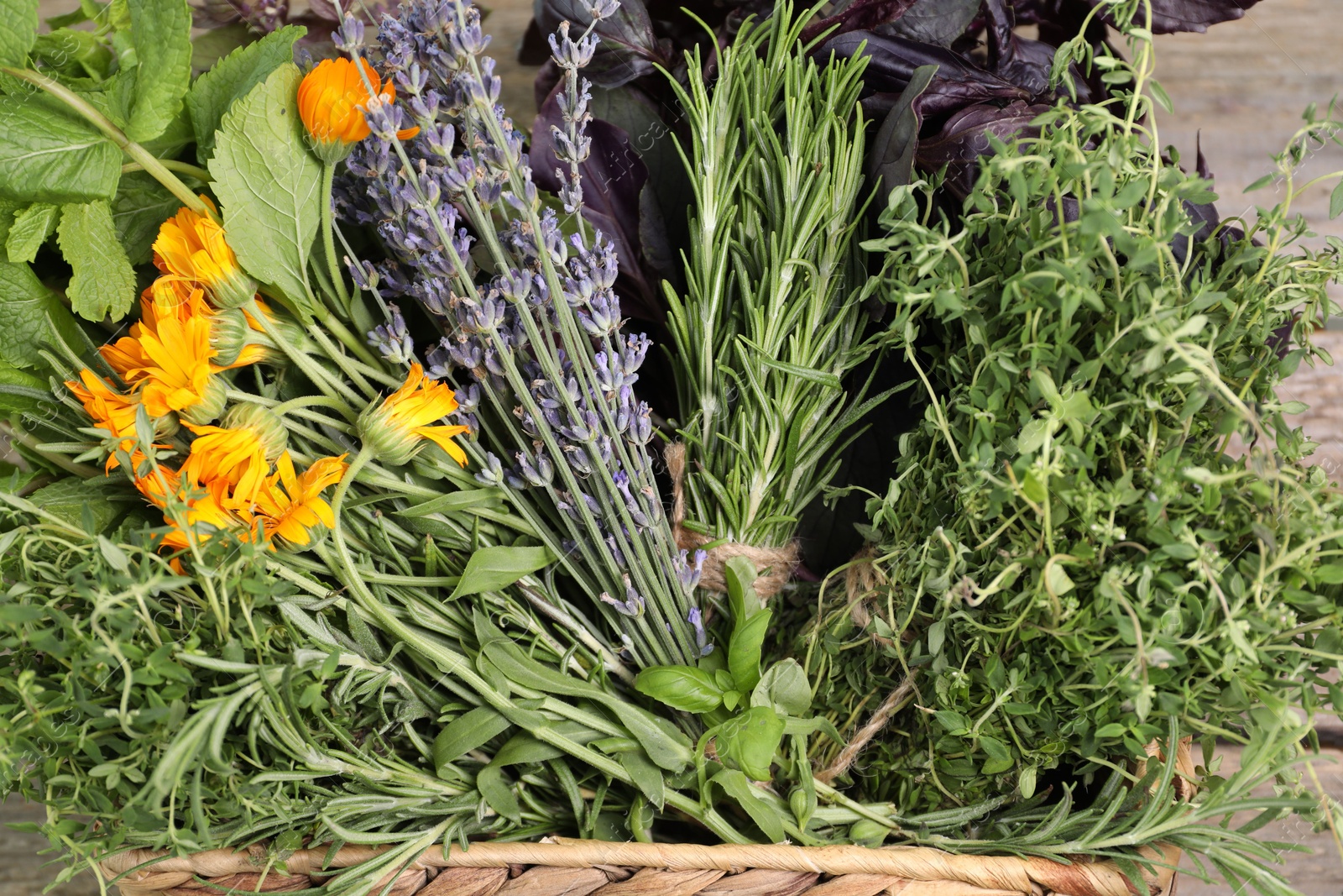 Photo of Different aromatic herbs in basket on wooden table, closeup