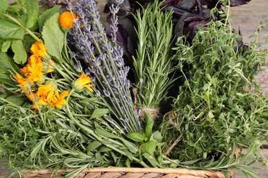 Photo of Different aromatic herbs in basket on wooden table, closeup