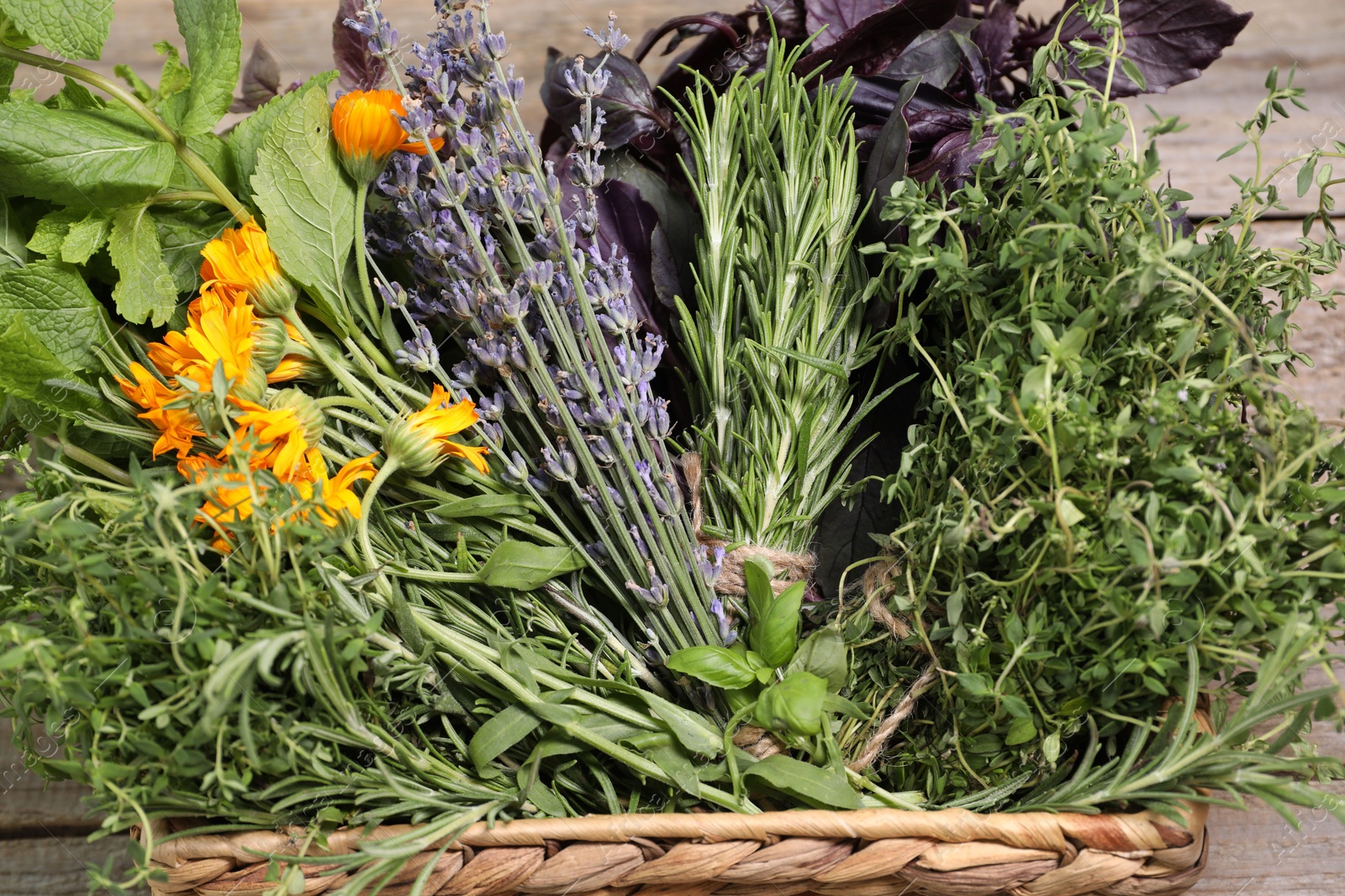 Photo of Different aromatic herbs in basket on wooden table, closeup