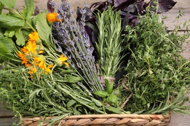 Different aromatic herbs in basket on wooden table, closeup