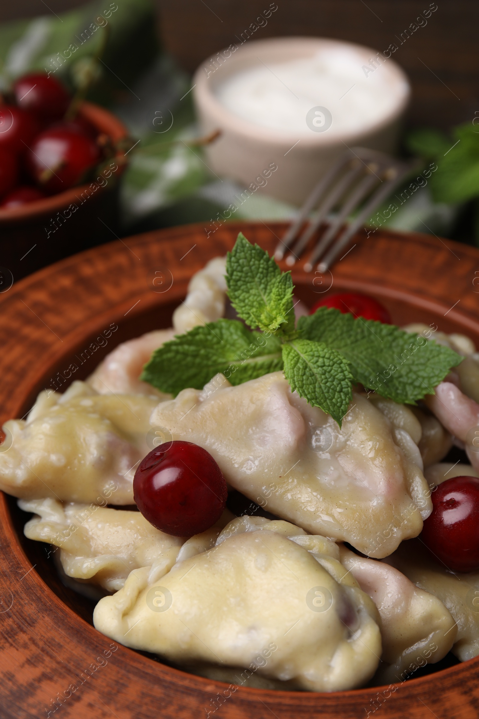 Photo of Traditional Ukrainian dumplings (varenyky) with cherries served on wooden table, closeup