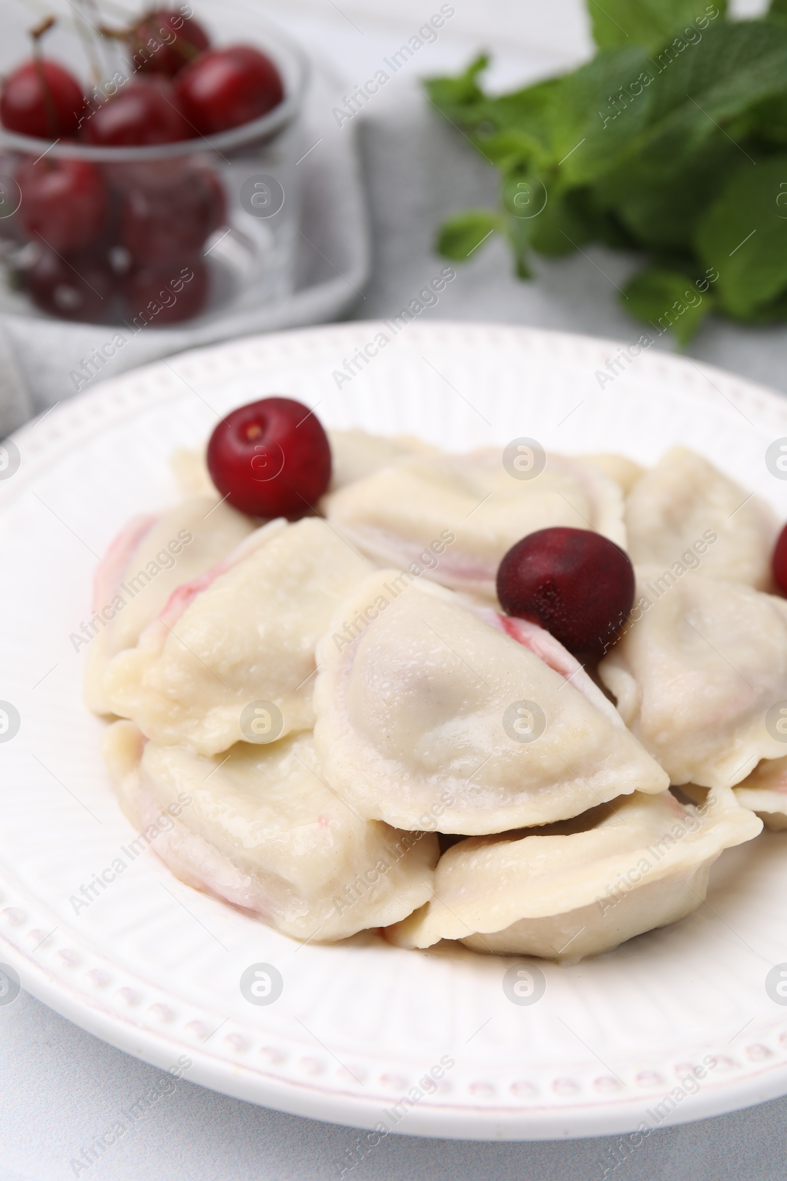 Photo of Traditional Ukrainian dumplings (varenyky) with cherries served on white table, closeup