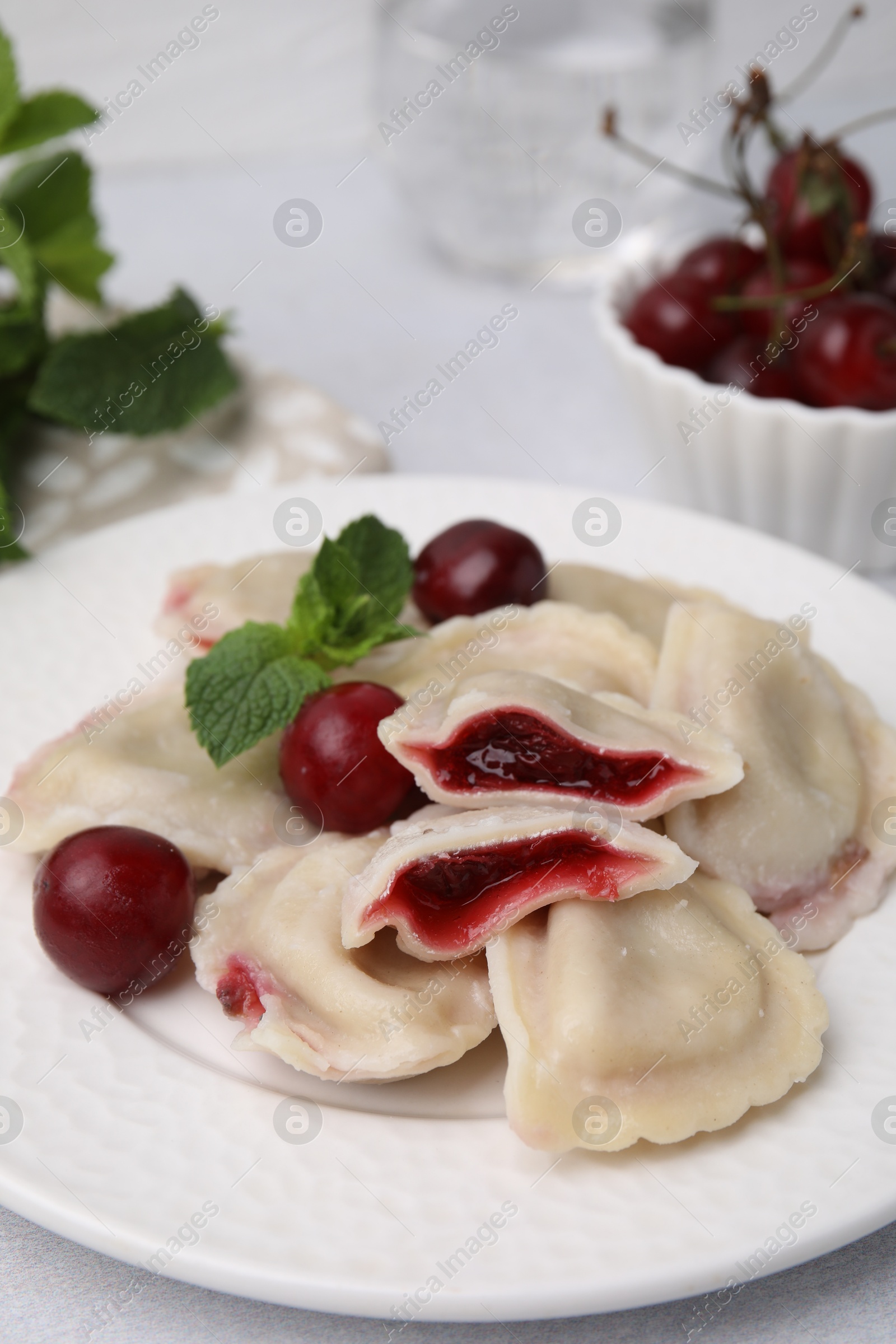 Photo of Traditional Ukrainian dumplings (varenyky) with cherries served on light table, closeup