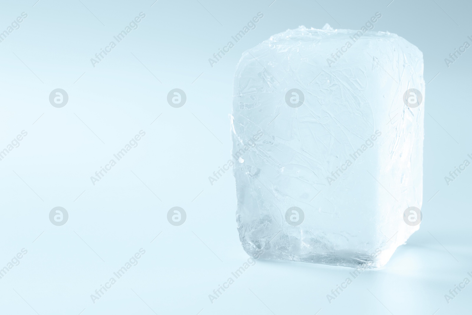 Photo of Cube of clear ice on light blue background, space for text