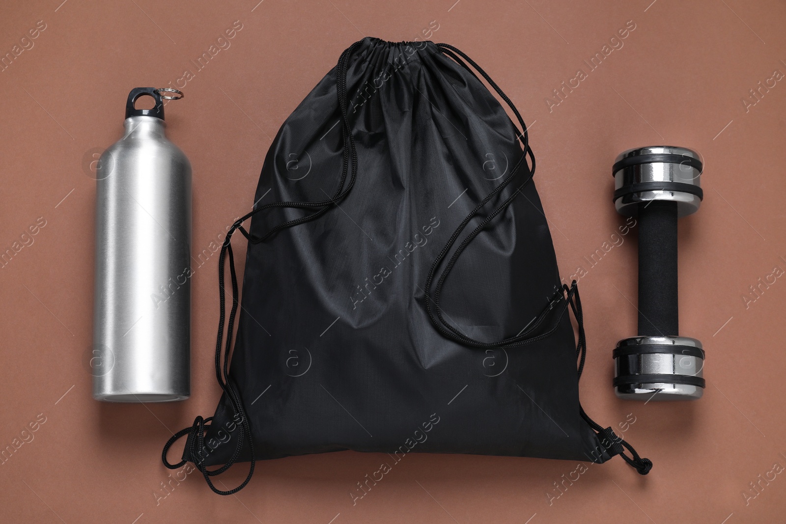 Photo of Black drawstring bag, thermo bottle and dumbbell on brown background, flat lay