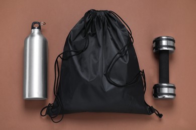 Black drawstring bag, thermo bottle and dumbbell on brown background, flat lay