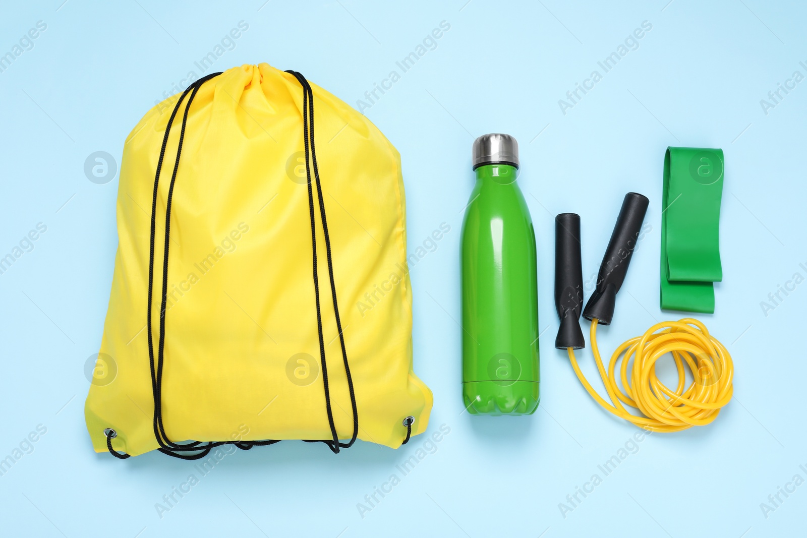 Photo of Yellow drawstring bag, thermo bottle, skipping rope and fitness elastic band on light blue background, flat lay