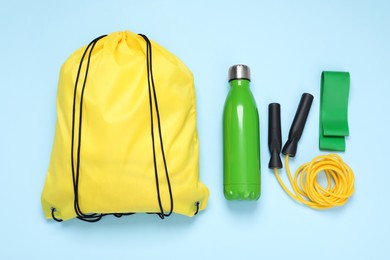 Yellow drawstring bag, thermo bottle, skipping rope and fitness elastic band on light blue background, flat lay